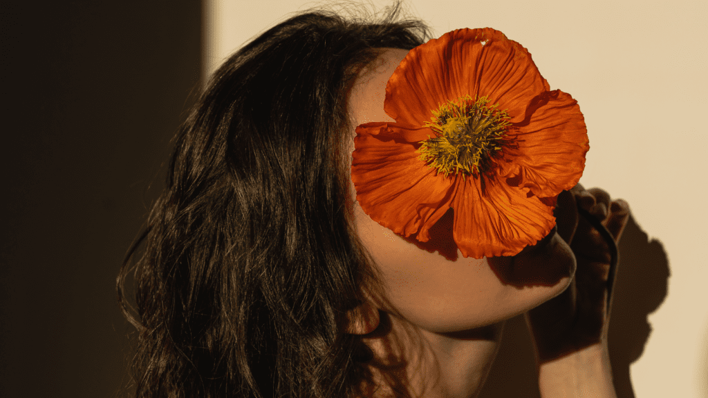 אישה עם פרח כתום על פנים כהמחשה לאדמומיות בפנים