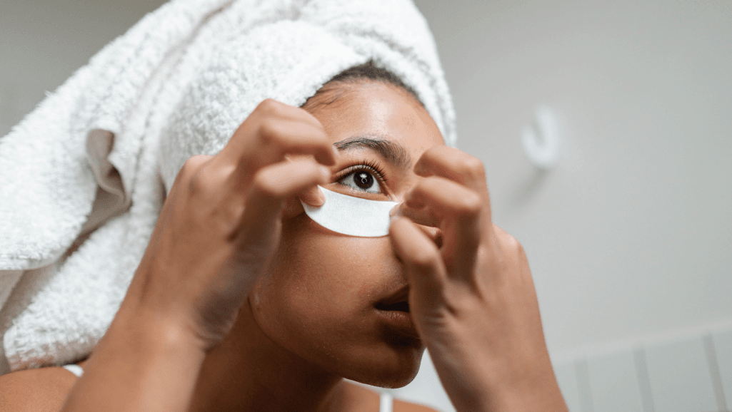 אישה מניחה מסכת עניים מתחת לעיניים עם מגבת על הראש